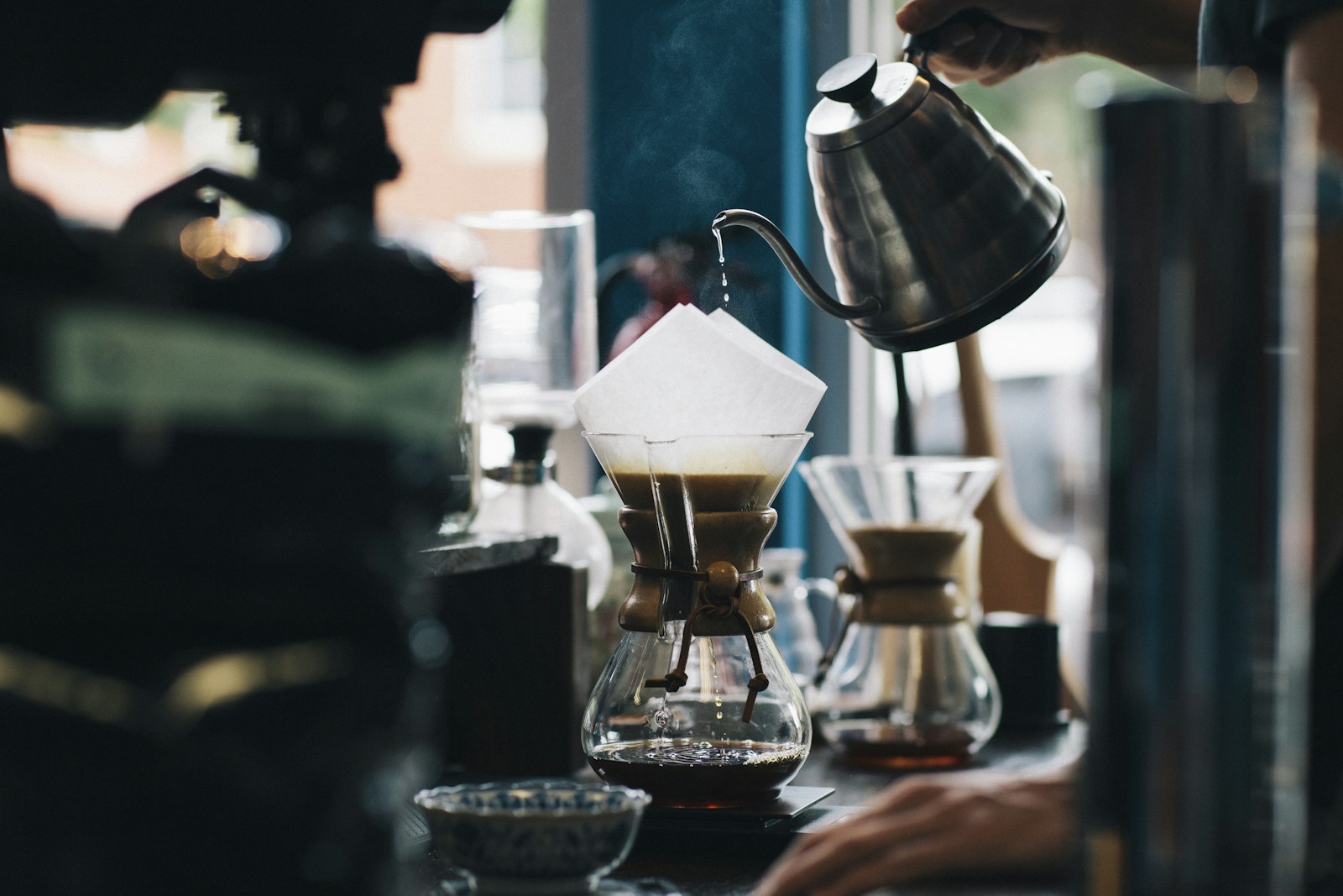 Gooseneck kettle pouring water through a paper filter into a glass Chemex coffee brewer