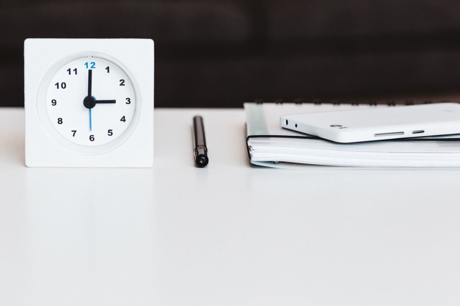 A white clock beside a notebook and phone on a tidy desk